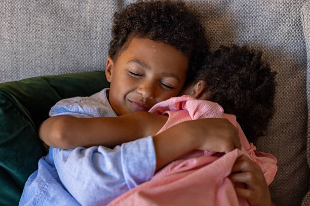 Two young siblings embracing each other while they both take a nap on the sofa of their living room in the North East of England. They have their eyes closed as they rest.Videos are available similar to this scenario.