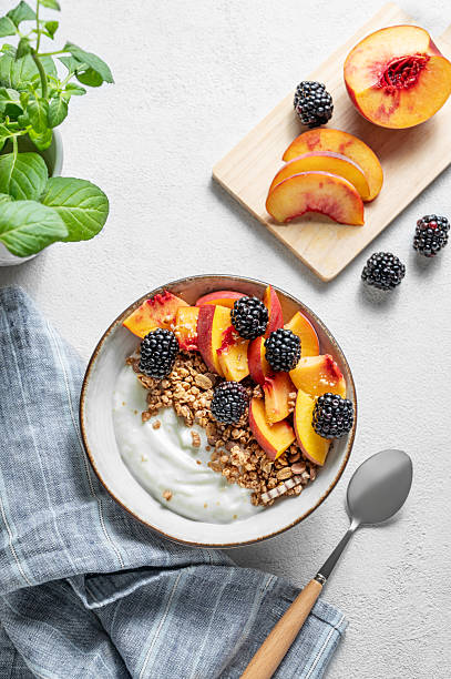 Natural greek yogurt with granola, peach and blackberry in a bowl on a light background