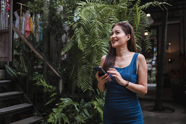 istock Young Asian woman using smartphone smiling in garden cafe 2239588551