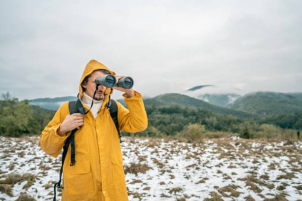 istock Man in Yellow Raincoat With Binoculars Exploring Snowy Field and Mountain Landscape 2239591166