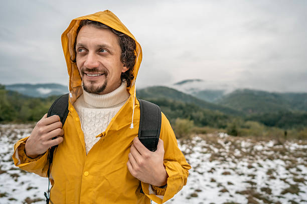 istock Smiling Man in Yellow Rain Jacket With Backpack Outdoors on a Snowy Mountain Field Today 2239591168