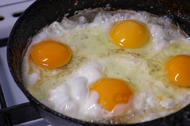 This appetizing close-up shows four bright egg yolks and cooking egg white in an old, hot frying pan. It is a perfect shot to illustrate themes of breakfast, simple cooking, home cuisine, and concepts of healthy eating or starting the day.