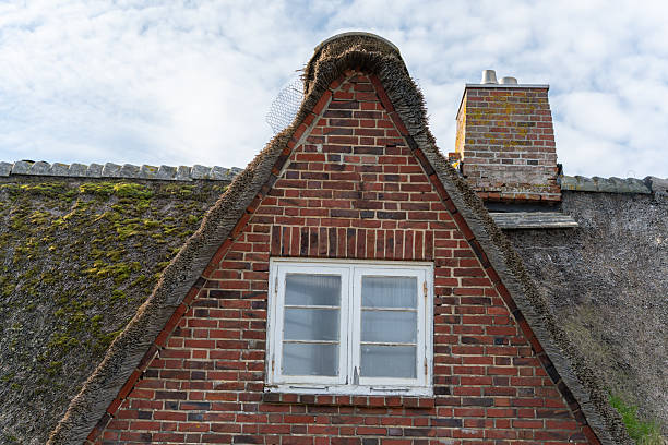 A red-brick gable house with a thatched roof and white-framed windows.