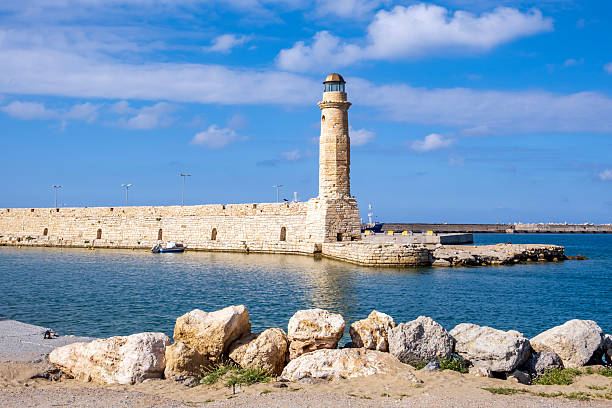 harbor and lighthouse of the city of rethymno in in crete greece , with boats, reflexions on the waves of the sea and clouds