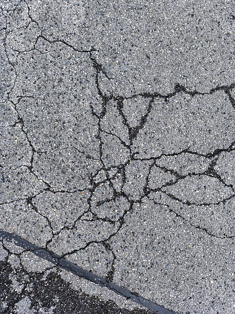 istock Close up of weathered asphalt pavement with severe spider web cracks texture 2239602650