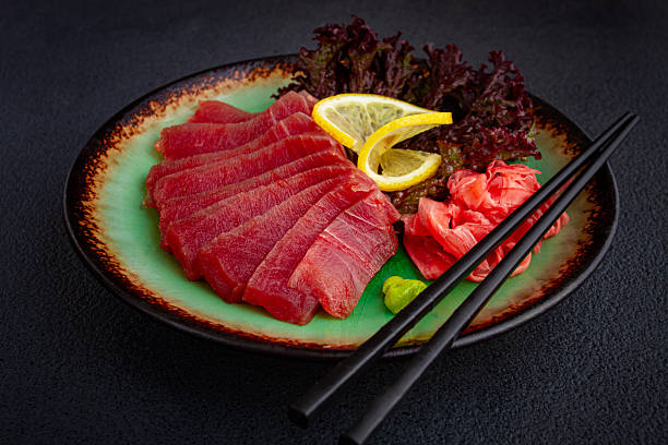 istock Fresh tuna sashimi served with lemon, wasabi, and pickled ginger on a dark background 2239604265