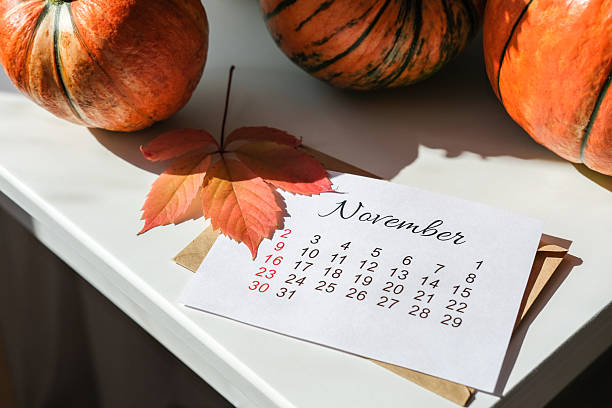istock Close-up of a November calendar sheet and a single fall leaf resting on white table with three orange pumpkins. Seasonal change, planning for autumn holidays 2239604764