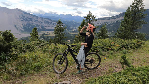 istock Woman mountain biker drinks water on mountain top 2239607475