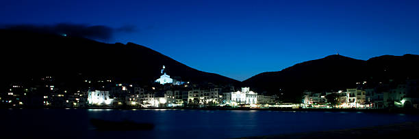 Cadaques town reflecting light onto the tranquil Mediterranean Sea at night, showcasing its iconic architecture and generating a peaceful tourism scene under a dark blue sky