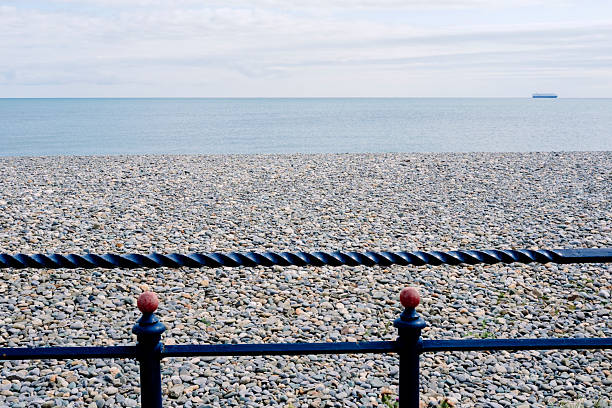 Explore the serene beach in Ireland, where smooth round pebbles meet calm waters under a soft, cloudy sky. A decorative railing adds a touch of elegance to the tranquil setting.