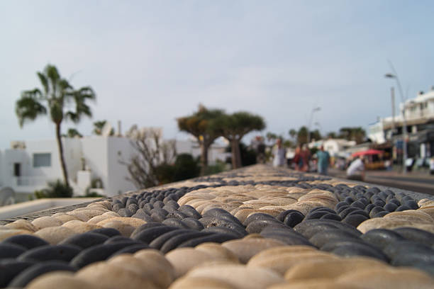 The volcanic coast of Playa Blanca in Lanzarote is lined by chains with love padlocks, palm trees and white villas. Tourists enjoy the ocean views and a romantic walk, blending natural beauty with local tradition.