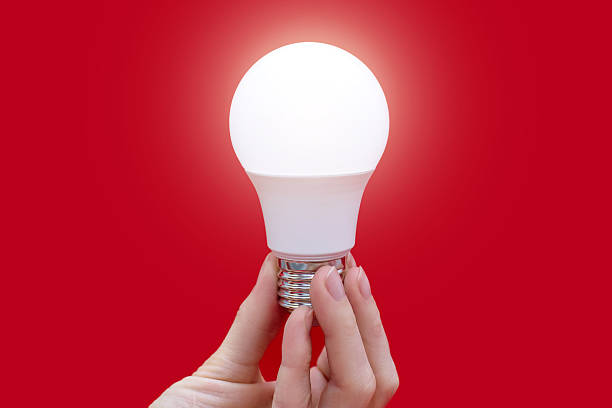 istock Glowing energy-saving light bulb in hand on a red background 2239633551