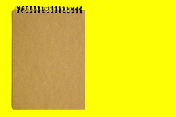 Notebook made of brown paper with a binding on a yellow background. Dark paper notepad with free space for text. Notepad with blank sheets of rough brown paper