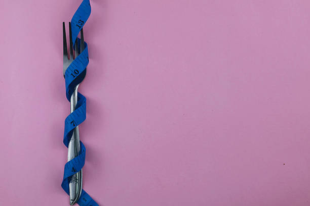 Stainless fork tied with twisted blue measuring tape isolate on pink background. Diet and fit body concept. Copy space.