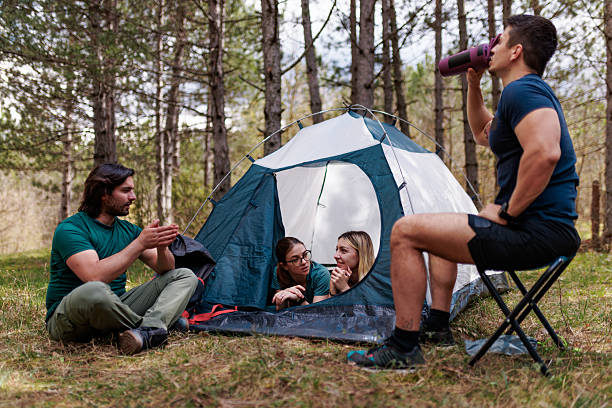istock Friends enjoying time together while camping in a forested area with a tent, sharing stories and beverages during a sunny afternoon 2239648441