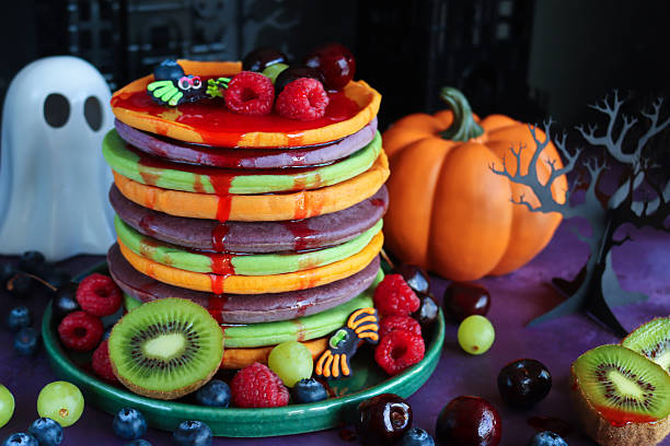istock Close-up image of Halloween food, multicoloured pancake stack with fresh fruit, alternating orange, purple, green layers of flapjacks, raspberry, blueberry, dripping strawberry sauce, fondant spiders, ghost, pumpkin, 3D paper craft tree, spooky houses 2239649326