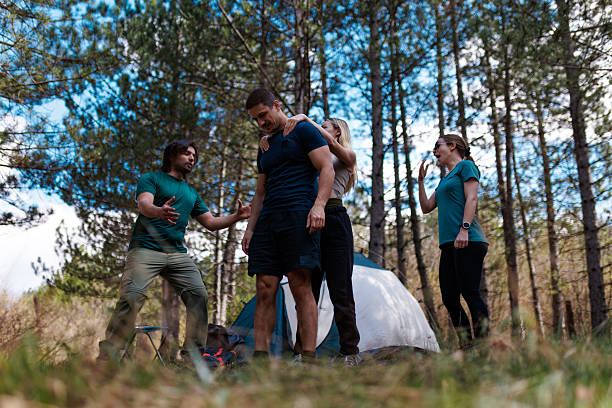 istock Group of friends enjoying a camping trip in the forest while setting up their tent surrounded by trees on a sunny day 2239652737