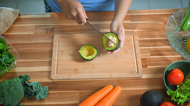 istock Hands cutting avocado on wooden board surrounded by fresh vegetables, symbolizing healthy eating and clean food 2239662403
