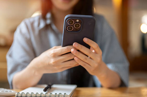 istock Close up of woman hold phone in both hands watching video or texting message over a notebook on cafe 2239664254