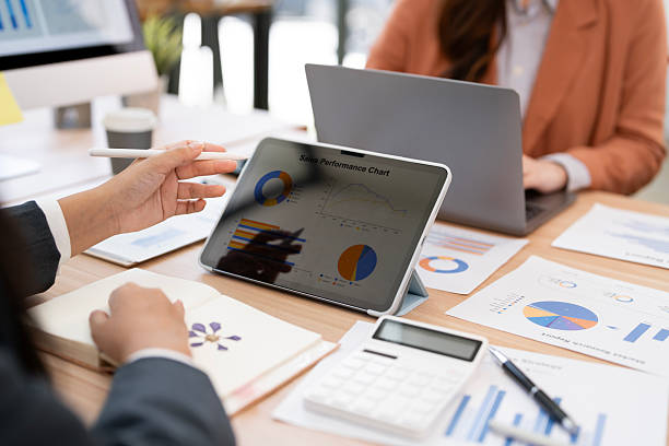 istock Two business professionals collaborating in a meeting, analyzing a performance chart on a digital tablet, surrounded by financial documents and tools on the desk. 2239669110