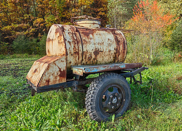 An old, rusty tank trailer sits in a field, surrounded by autumn foliage, showcasing a scene of rural decay and natural beauty.