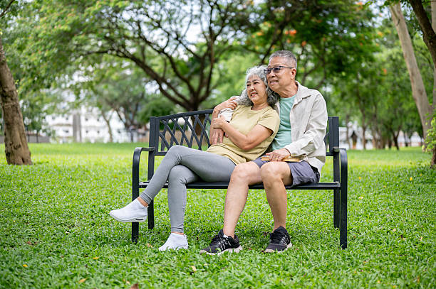 istock Glasses old man hugging old woman shoulder while sitting leaning against each other on bench in park 2239676373