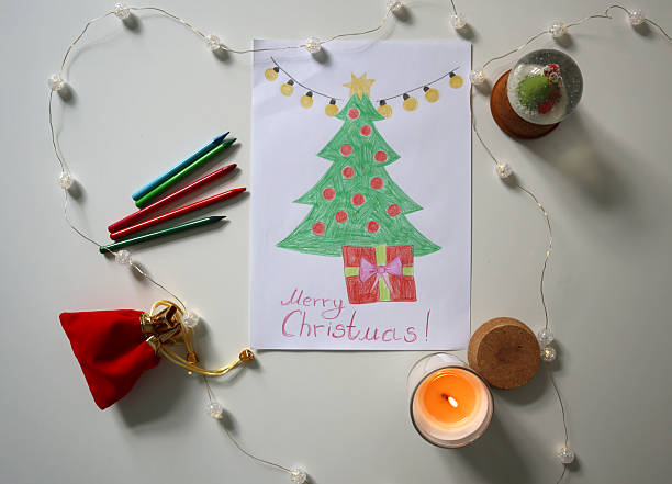 istock Flat lay of hand drawn Christmas tree with gift and Merry Christmas text, surrounded by crayons, candle, snow globe. 2239677610