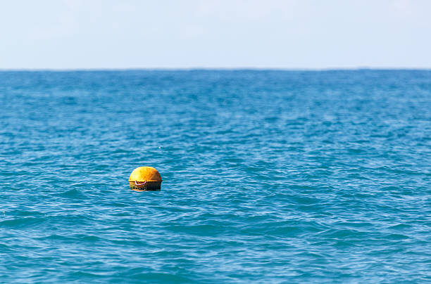 A yellow buoy is floating in the ocean. The water is blue and calm. The buoy is the only object in the water