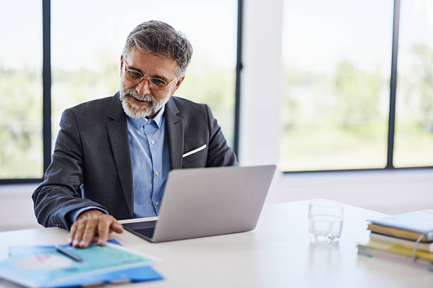 istock Smiling businessman working on laptop and reports in the office. 2239686385