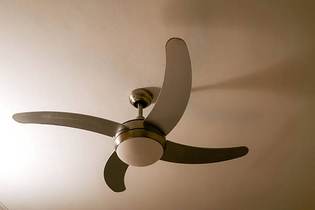 istock Modern Three-Blade Ceiling Fan Mounted on White Plaster Ceiling in Soft Warm Lighting, Minimalist Interior Detail 2239686495
