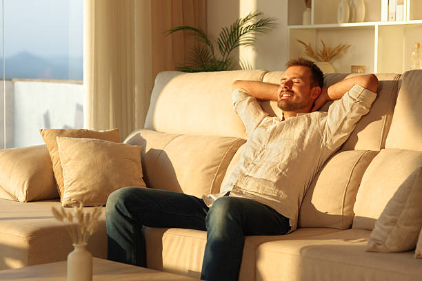 istock Happy man relaxing on a comfortable couch at sunset at home 2239687409