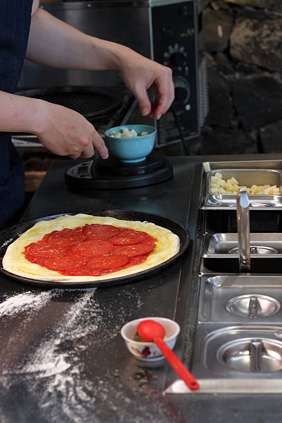 istock Chef spreading tomato sauce and arranging pepperoni on pizza dough 2239700439