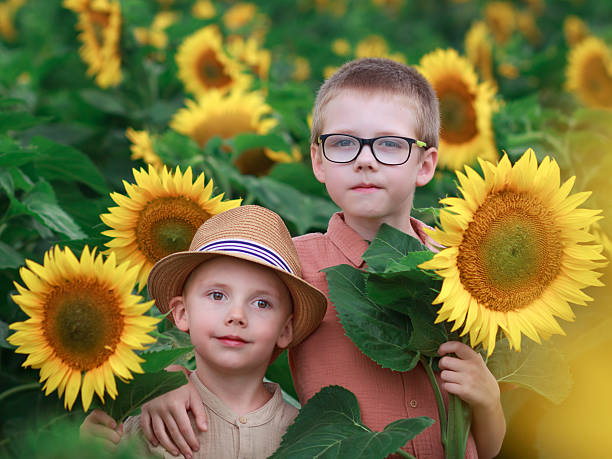 Two children stand among tall sunflowers in a green field. Concept of family, nature, and summer postcard.