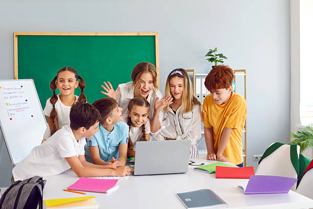 istock Group of happy school children and teacher using modern laptop computer in class 2239702388
