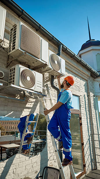 istock Worker on ladder maintaining multiple air conditioning units on building wall 2239705734
