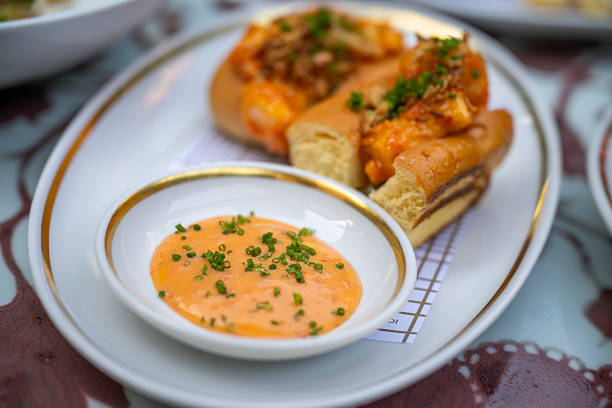 Close-up of gourmet prawn rolls topped with herbs and crispy onions, served with a creamy spicy dipping sauce on an elegant white plate at a stylish outdoor restaurant.