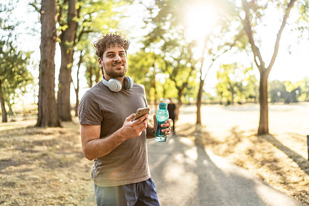 istock Young man holding phone and water bottle in park 2239724780