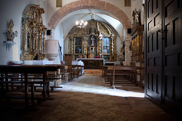 Man in white shirt sitting on a pew, bowing his head in prayer inside an ancient church with intricate golden altarpiece and sunlight shining on the floor
