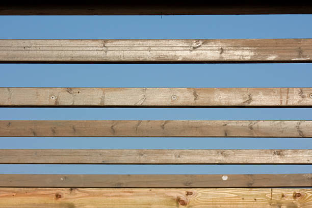 Parallel wooden slats creating a graphic pattern with gaps of clear blue sky, showing natural wood grain and texture, suitable for backgrounds or design elements