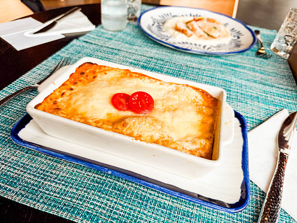 Baked lasagna with cheese crust and sliced tomato topping served on a table setting. Cuisine, dining, and homemade comfort food symbolizing tradition, taste, and culinary lifestyle