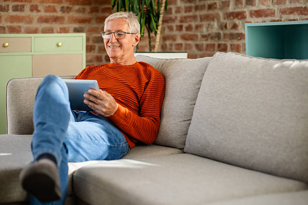 istock Cheerful senior man enjoying his leisure time at home while reading on a tablet in a cozy living room 2239732840