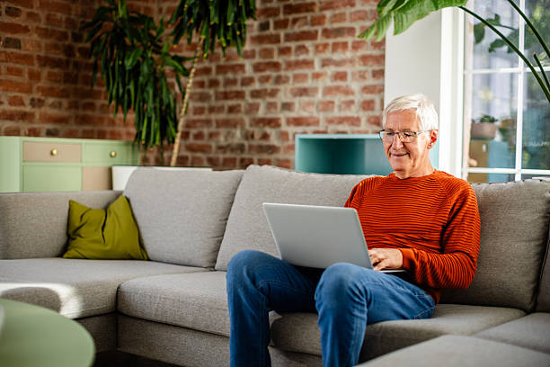 istock Senior man enjoying leisure time at home while using a laptop in a comfortable living room 2239734380