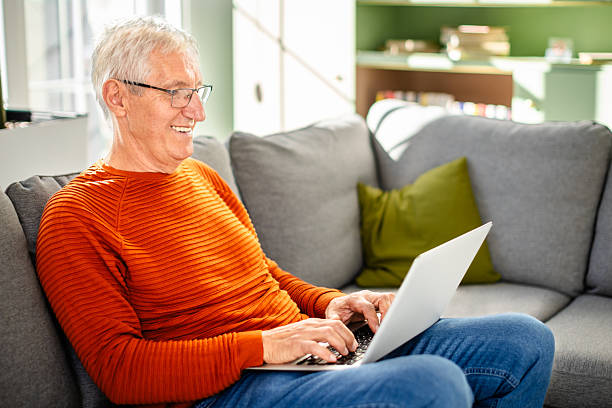 istock Senior man enjoying leisure time at home while using his laptop on a cozy sofa 2239734747