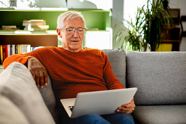 istock Senior man enjoying leisure time at home while using laptop in a comfortable living room 2239734806