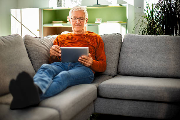 istock Senior man enjoys leisure time at home while using a tablet in a cozy living room setting, radiating contentment and relaxation 2239735376