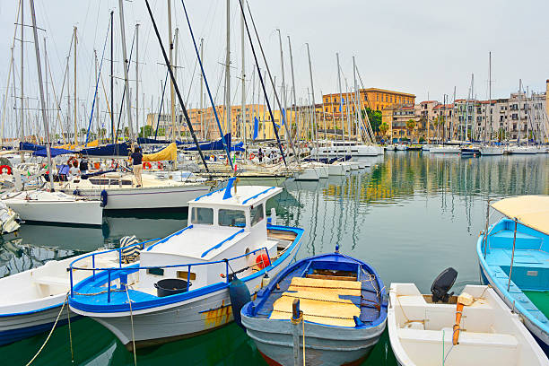 La Cala Marina in Palermo's Kalsa district, Sicily, Italy. Historically the city's port, now a picturesque marina. A vibrant and active marina, blending historical significance with contemporary leisure activities. A mix of recreational vessels catering to both sailing and fishing enthusiasts, it is home to thousands of motorboats and sailing yachts with tall masts. In the background, multi-storey residential buildings line the waterfront