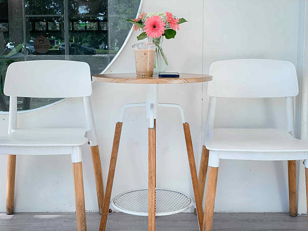 The image features two empty white chairs with natural wood legs, facing a small round wooden table.