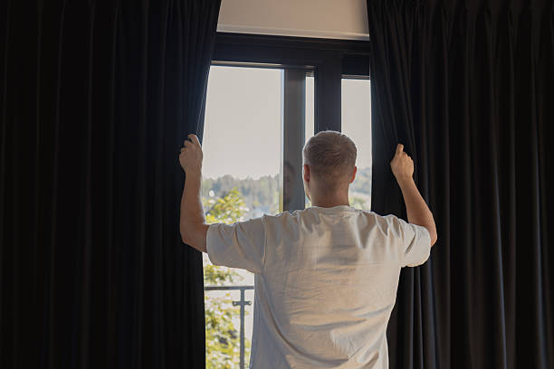 istock Man opening dark curtains on window to let sunlight in 2239740362