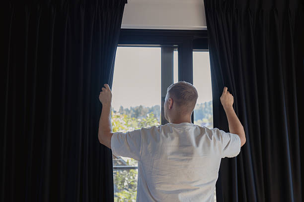 istock Man opening dark curtains on window to let sunlight in 2239740524