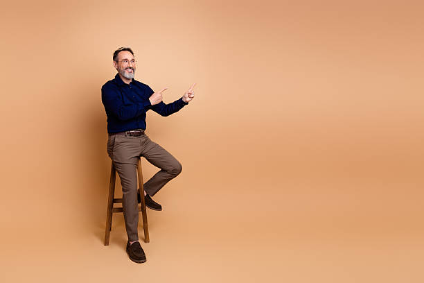 istock Confident businessman sitting on a stool demonstrating hand gestures against a beige background in a formal setting 2239741306